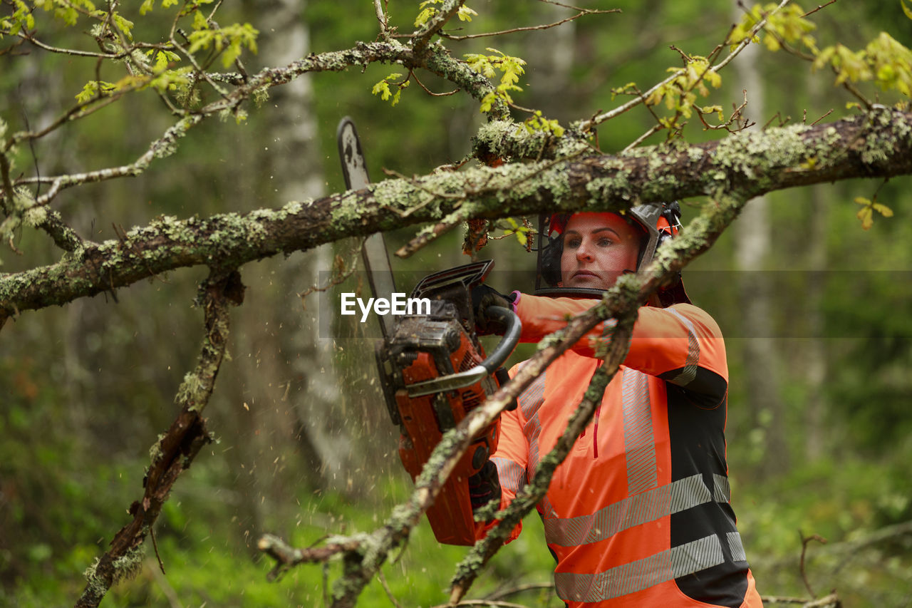 Female lumberjack cutting tree branch in forest