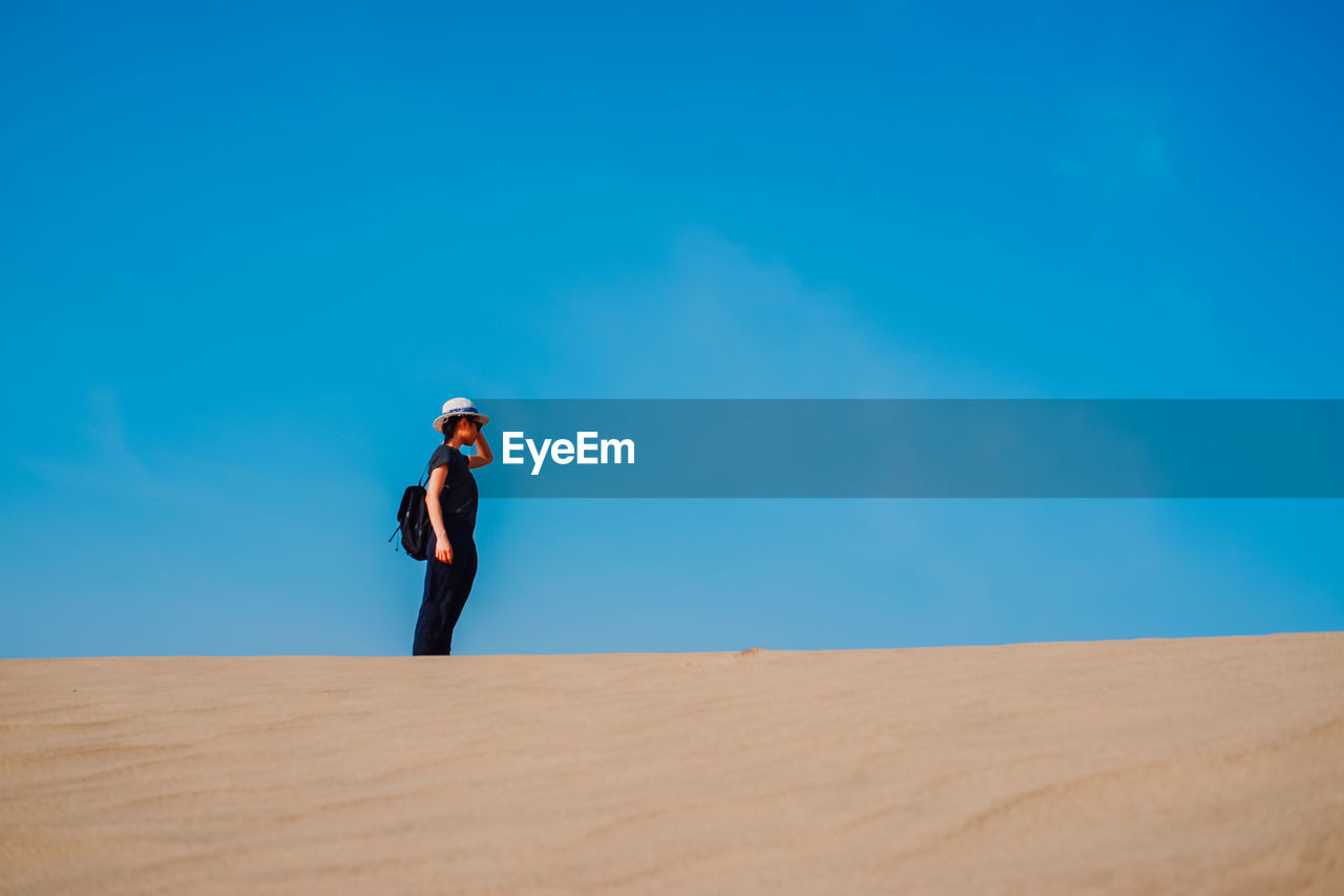 Woman standing on desert against blue sky
