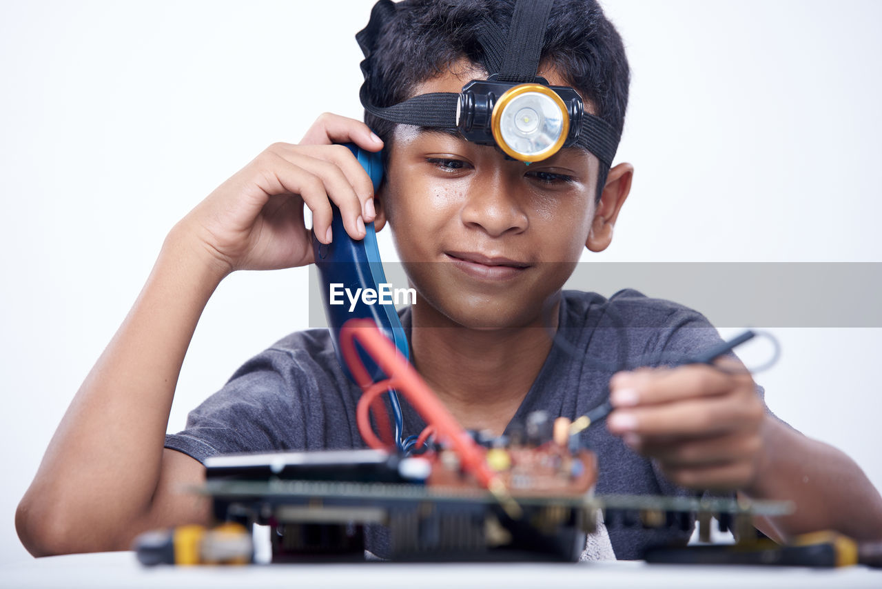 Schoolboy holding a landline phone and voltmeter to studying electronic telecommunication