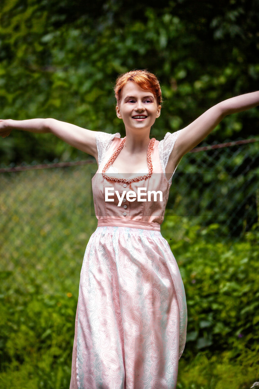 PORTRAIT OF A SMILING YOUNG WOMAN WITH ARMS RAISED