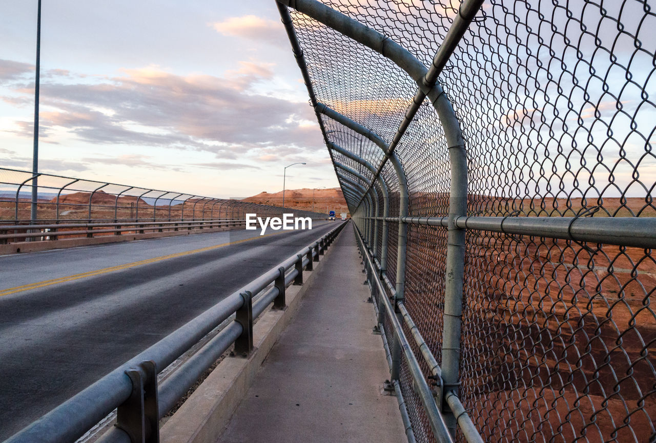Chainlink fence by road against sky