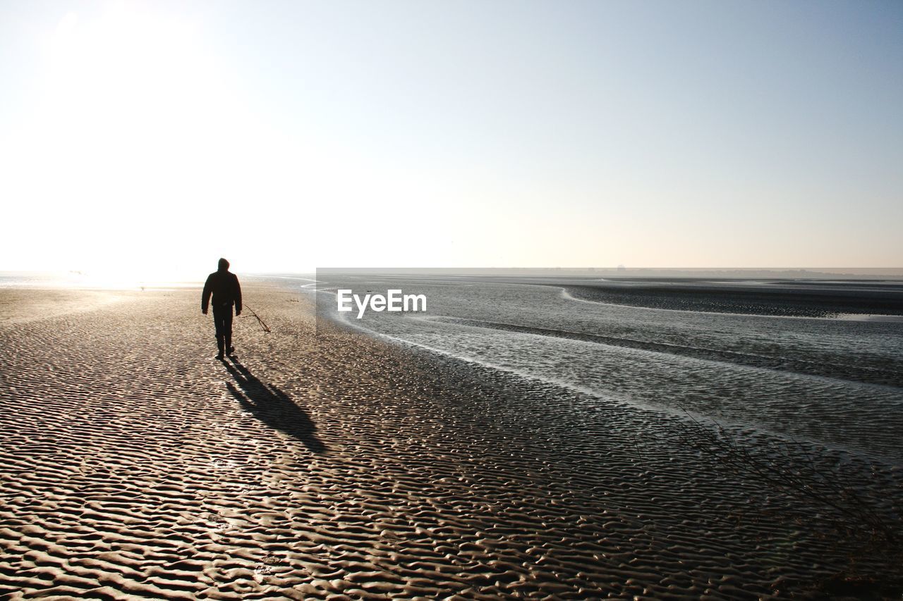 Rear view of silhouette man walking at beach against clear sky during sunset