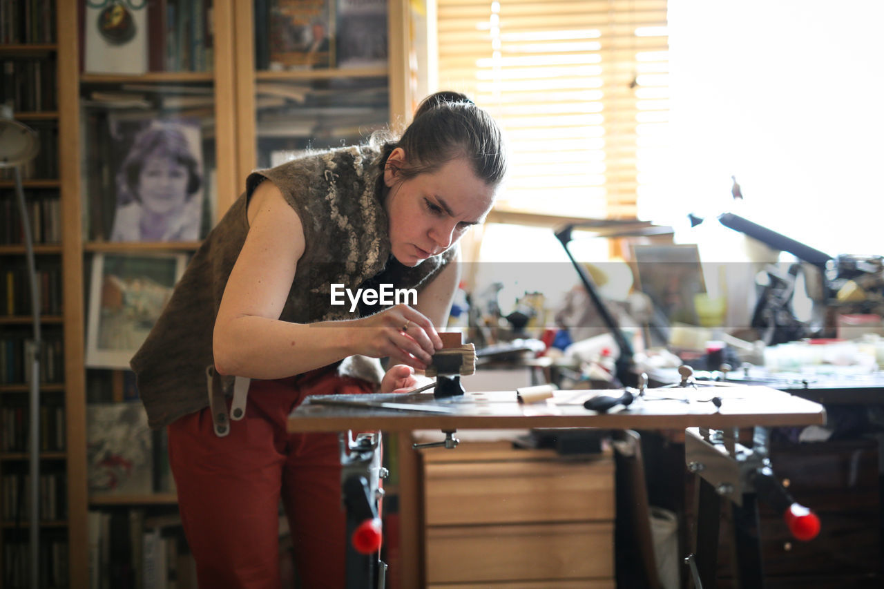 Girl master processes the metal copper plate on the workbench in the home workshop, soft focus 