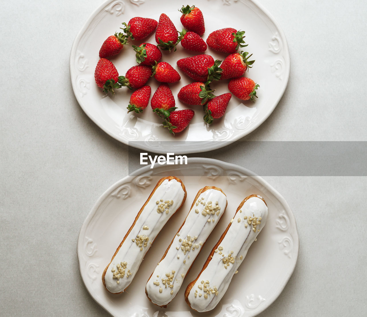 White glazed eclairs served with strawberries on two plates on white background, top view
