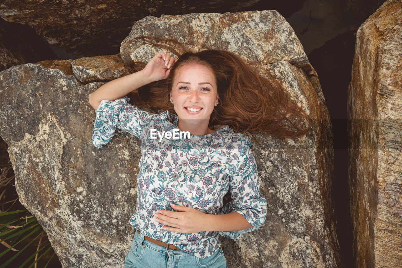 Portrait of smiling young woman lying down on rock