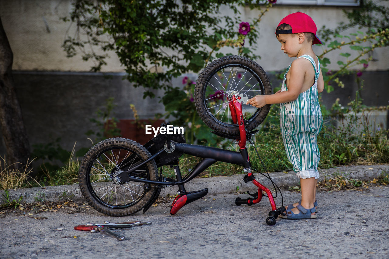 Side view of boy standing by bicycle