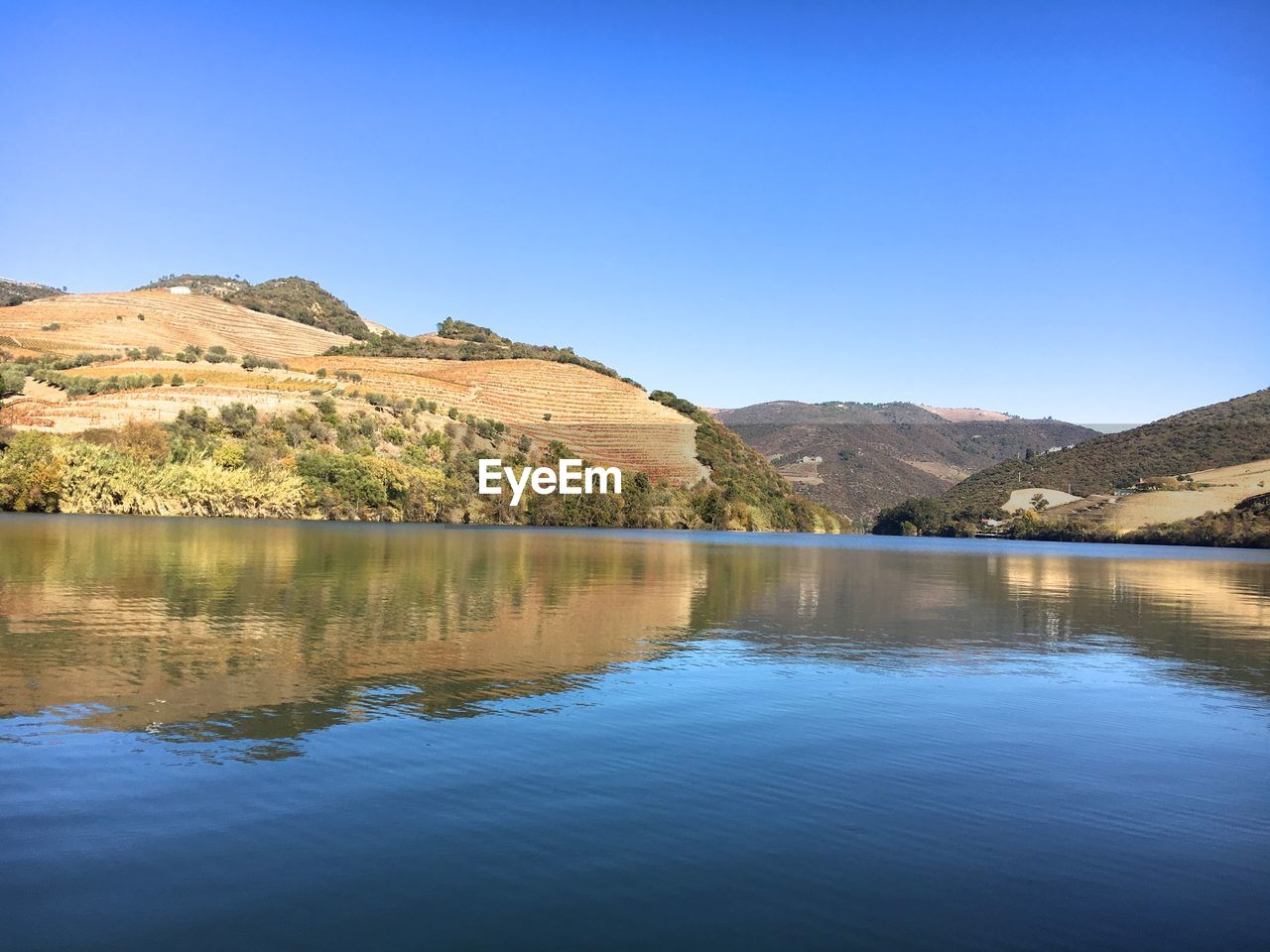 Scenic view of river by mountains against clear blue sky