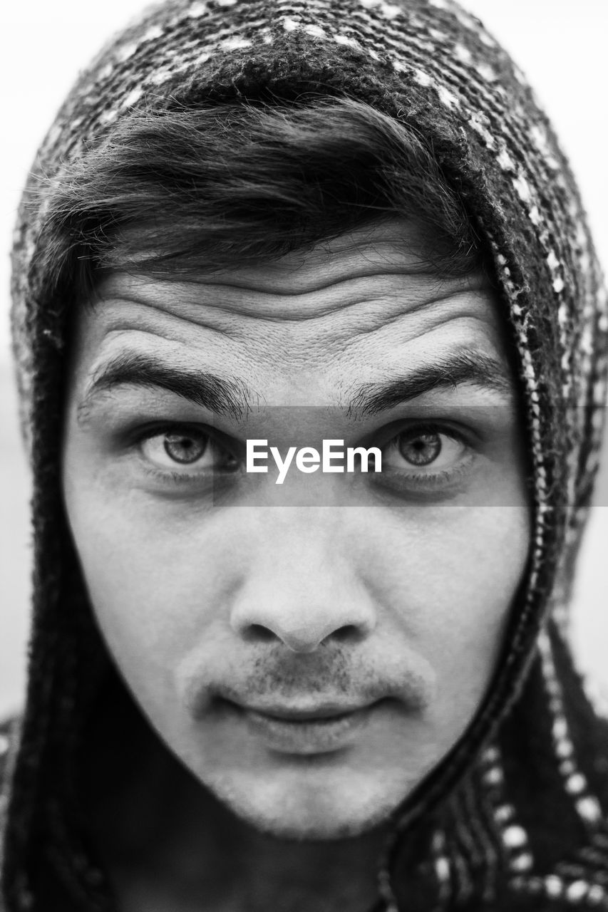 Close-up portrait of young man in hooded shirt against sky