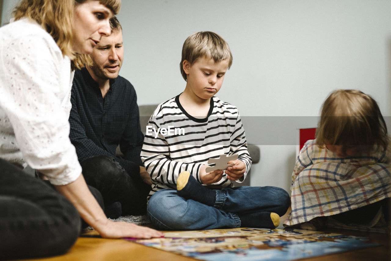 Boy having disability joining jigsaw pieces sitting with family at home