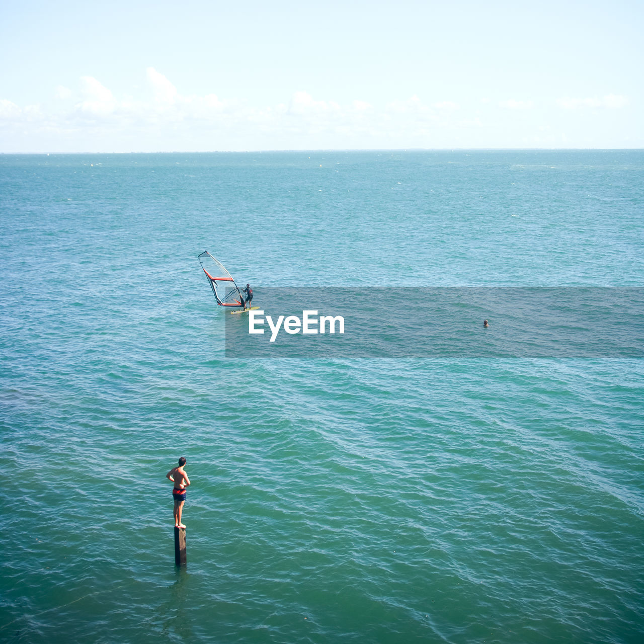 Boy looking at person windsurfing in sea against sky