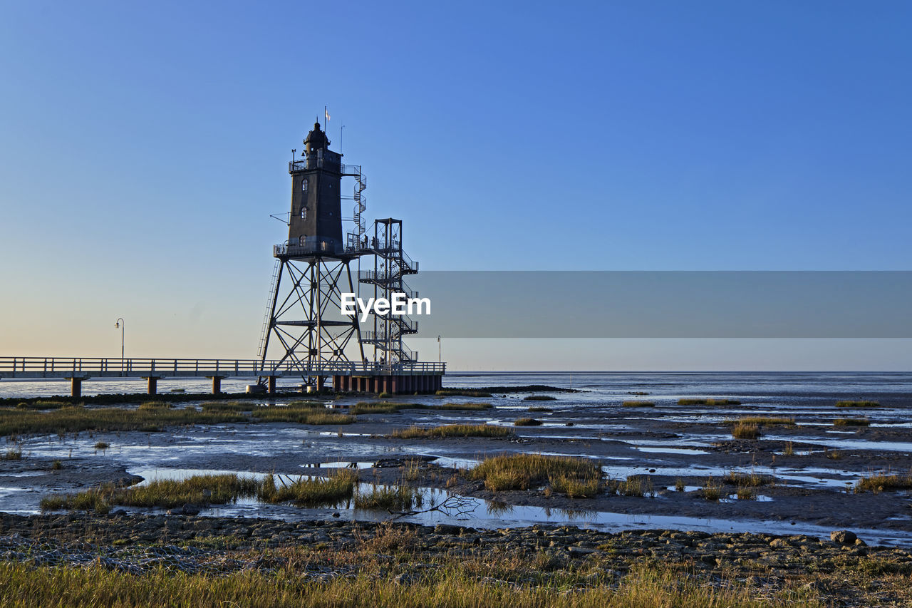 Lighthouse by sea against clear sky