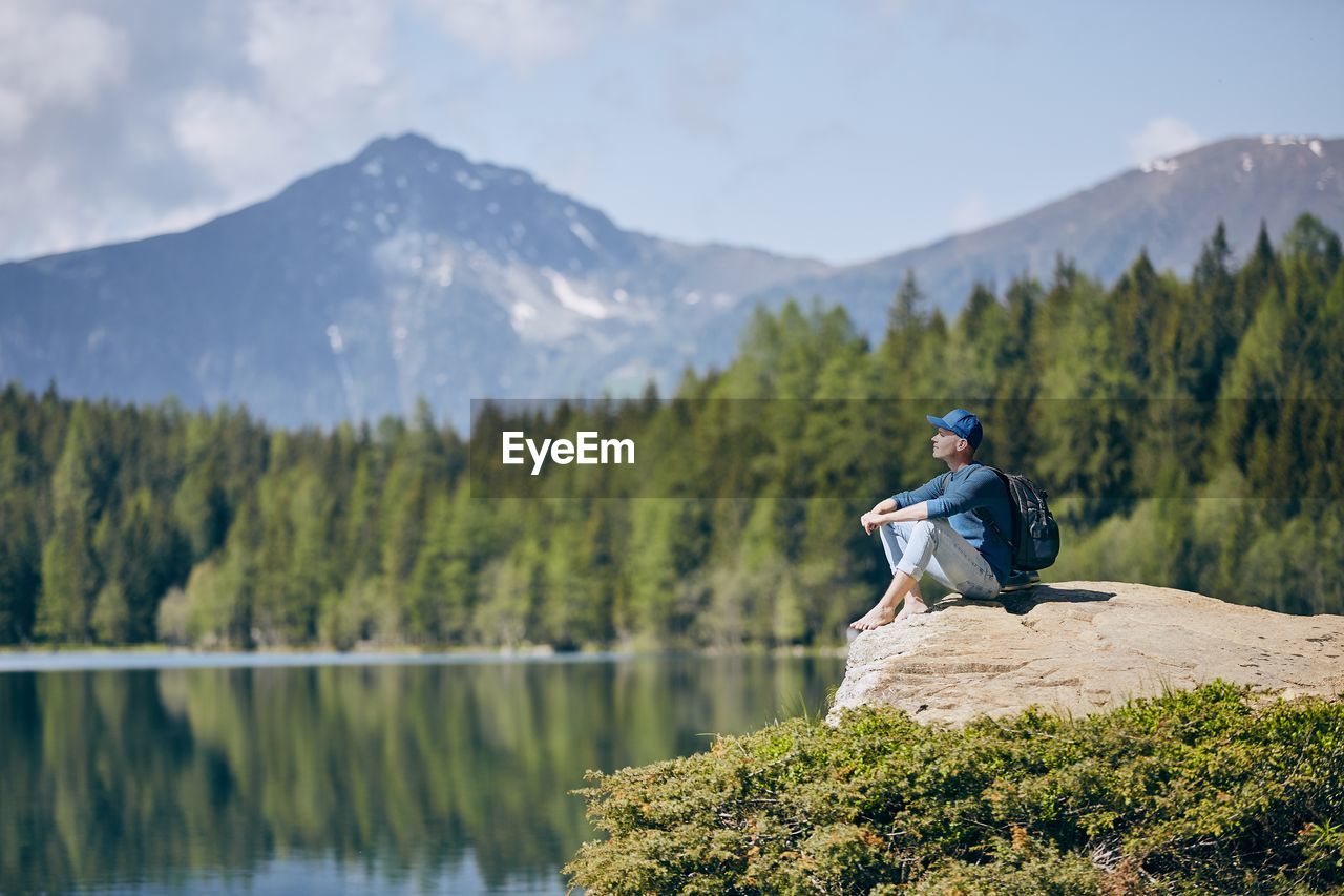 Hiker sitting on rock formation by lake against mountain