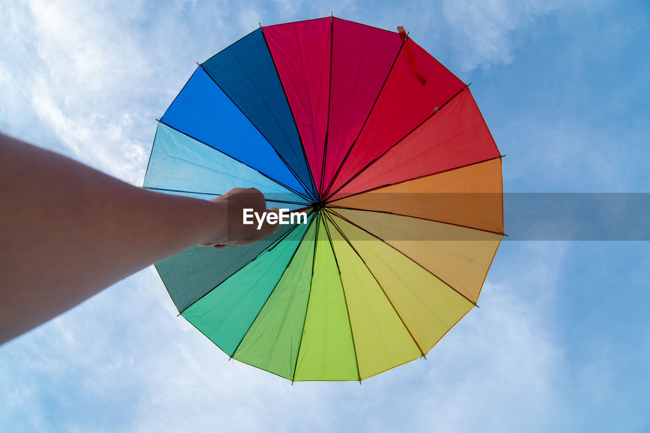 Human hand holding multicolored umbrella against sky