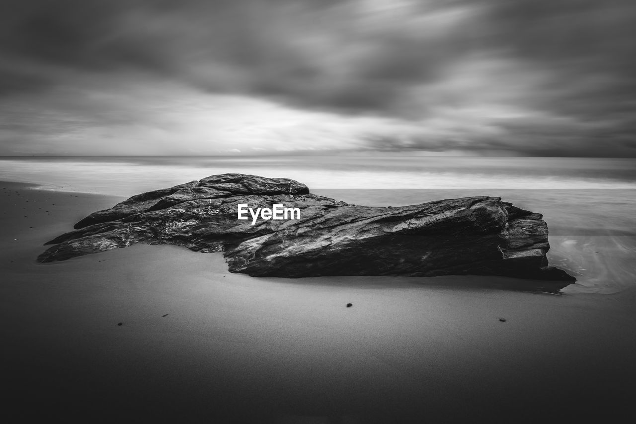 Rock formation at beach against cloudy sky