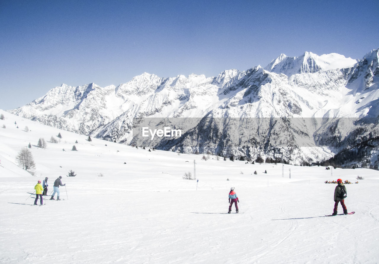 People skiing by snowcapped mountain against sky
