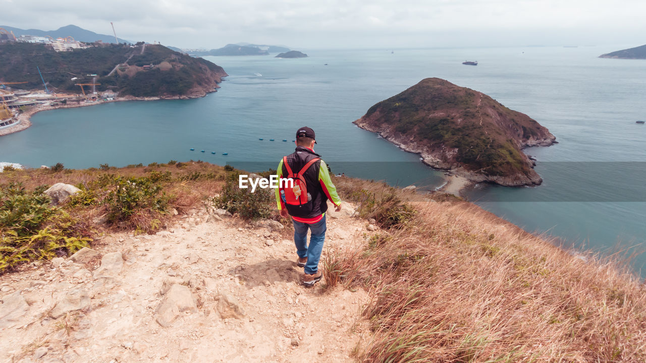 MAN STANDING ON ROCKS BY SEA