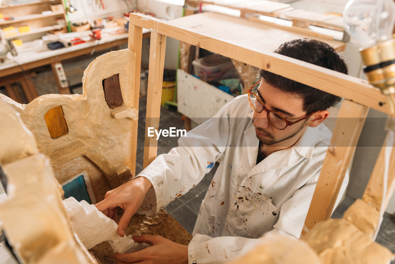 From above of focused male artisan creating facade of clay building while working in art studio