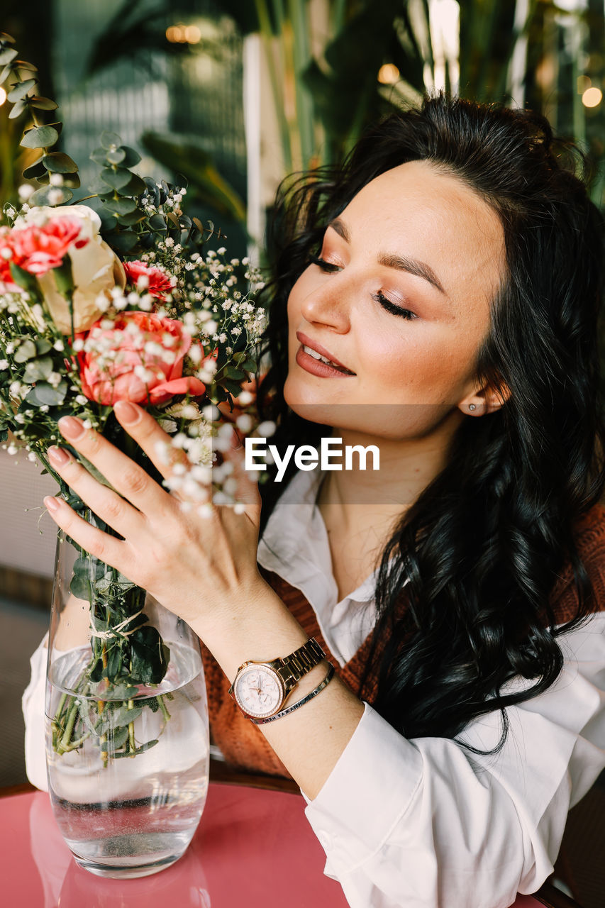 Portrait of a gentle attractive beautiful young brunette woman enjoying the smell of flowers