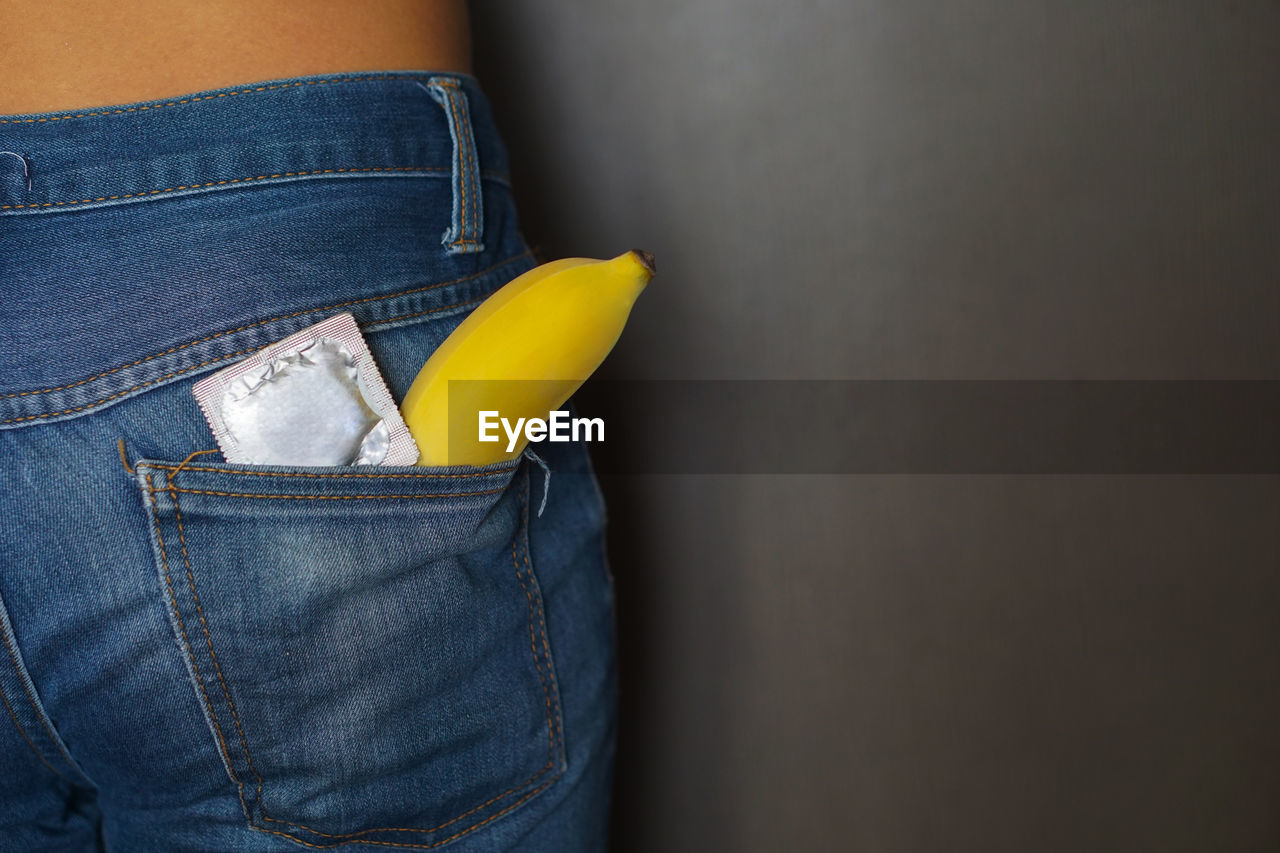 Midsection of man with condom and banana in jeans pocket