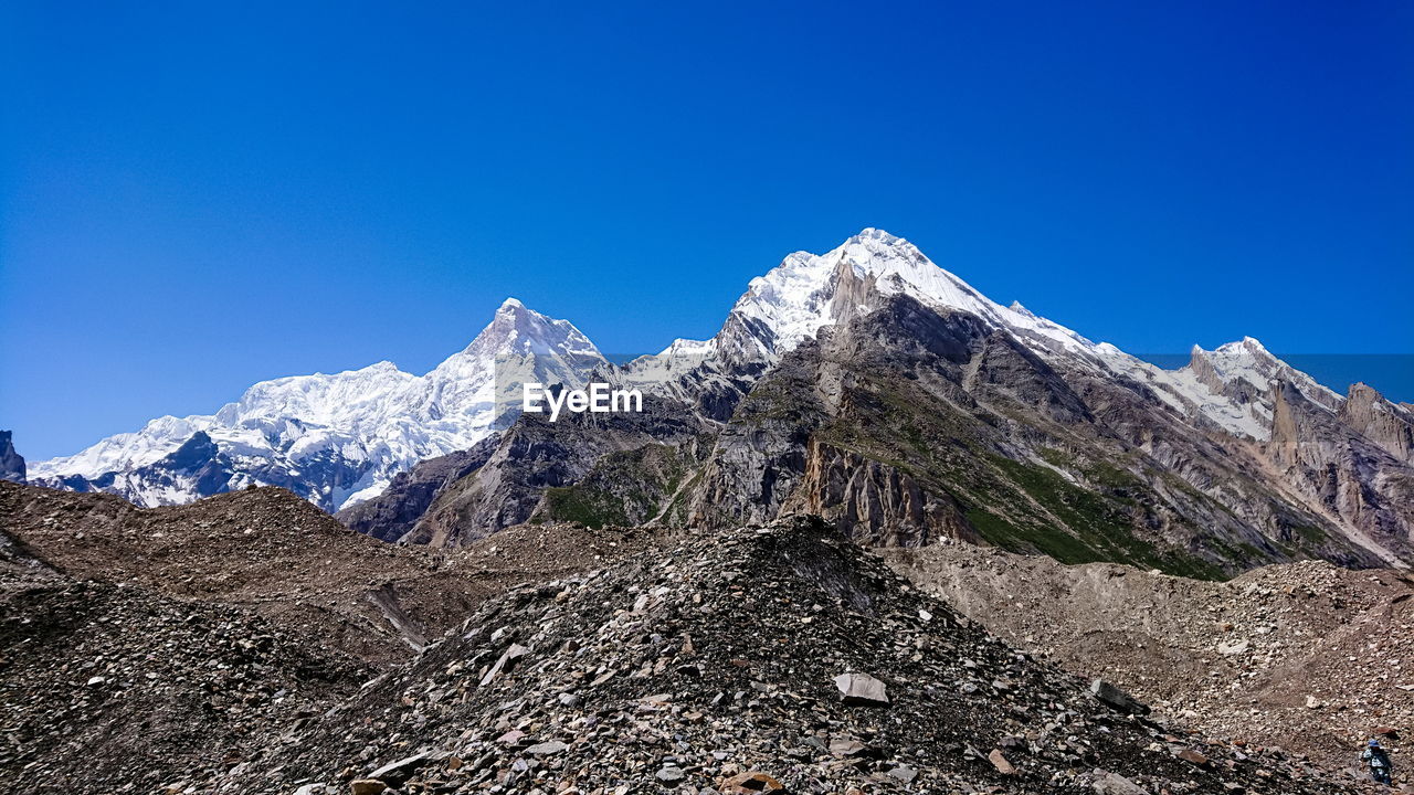 Low angle view of snowcapped mountains against clear blue sky