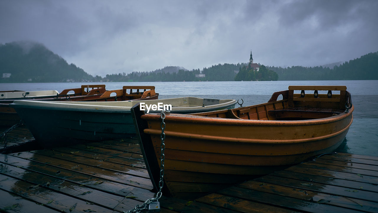 Boats moored on pier over lake against sky