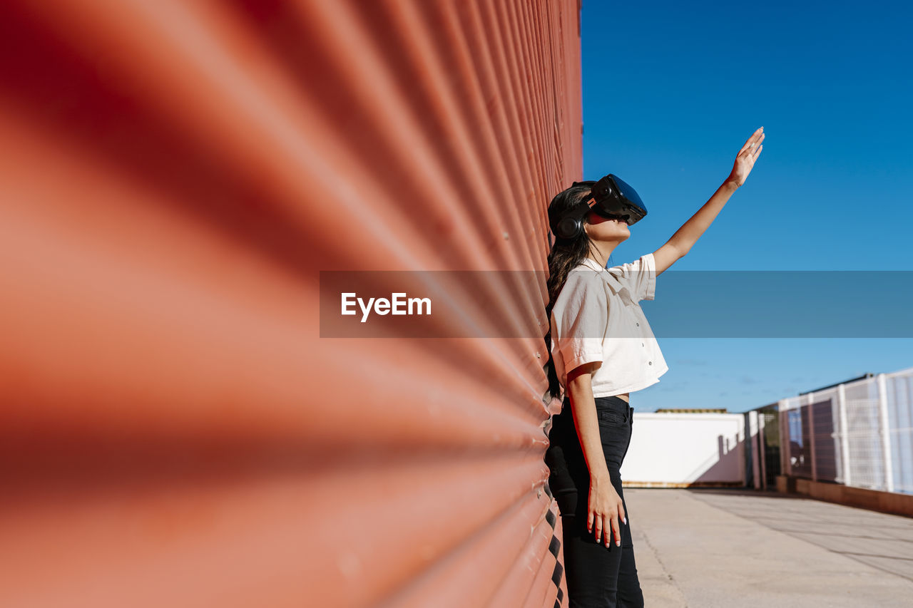 Young woman with virtual reality headset leaning on red wall