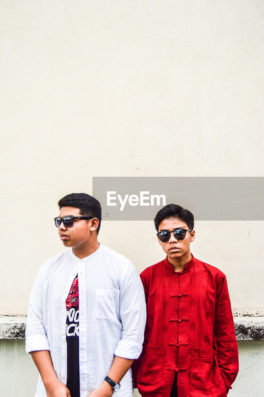 Male friends wearing sunglasses standing against wall