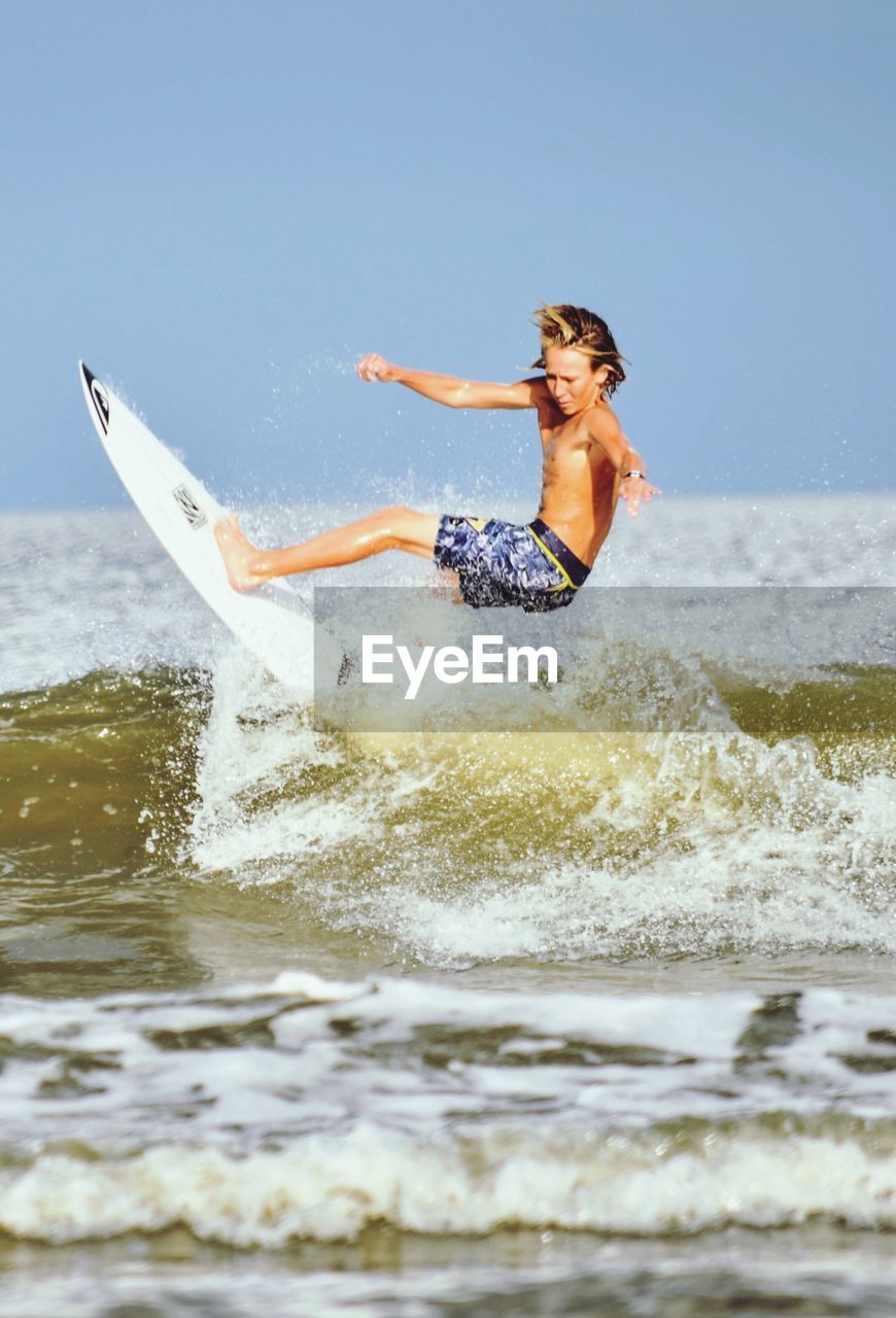 Shirtless boy surfing in sea