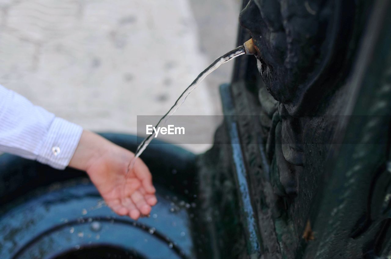 Cropped hand of person holding water falling from fountain