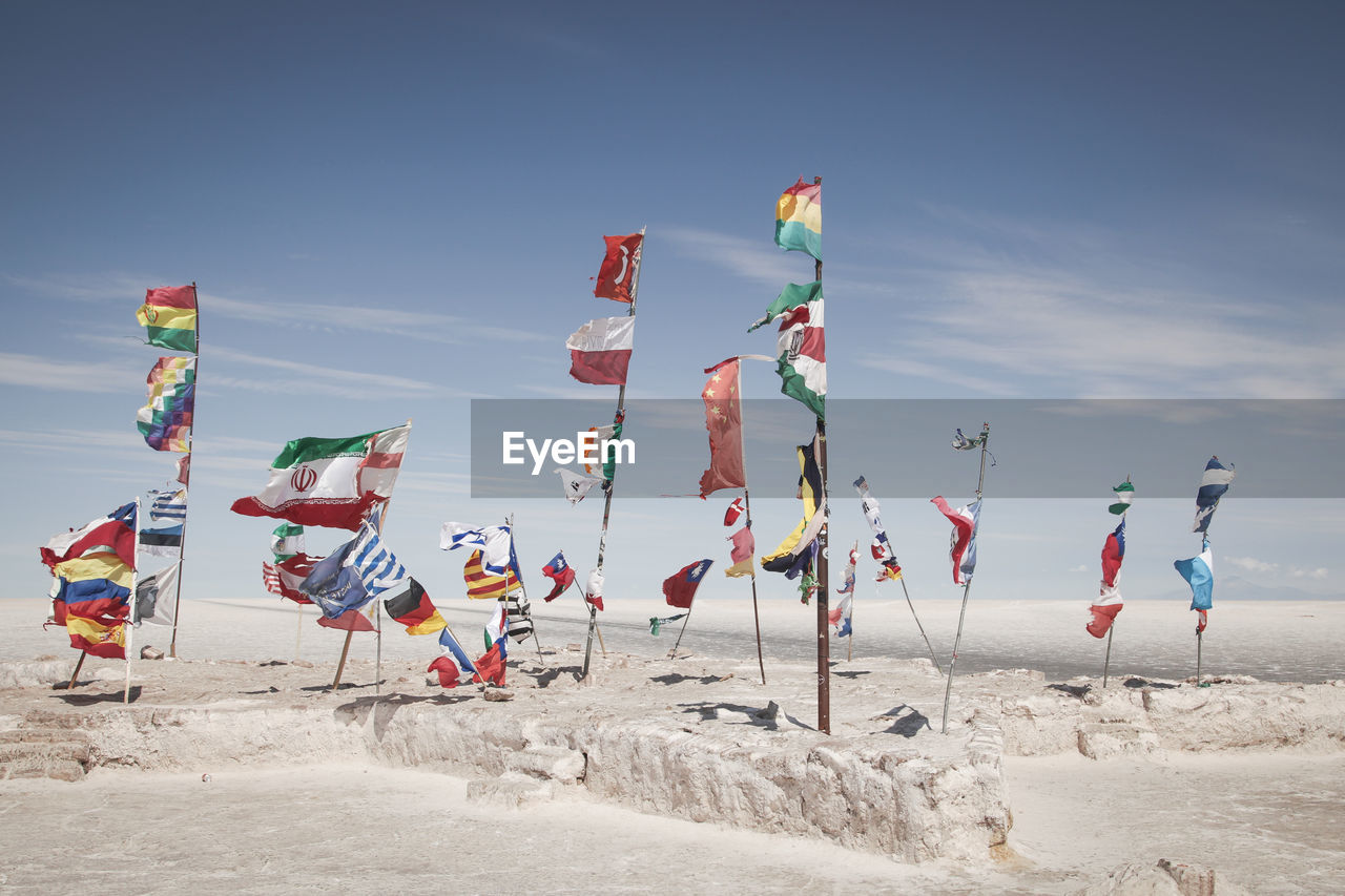 Various flags waving on salt flat against sky