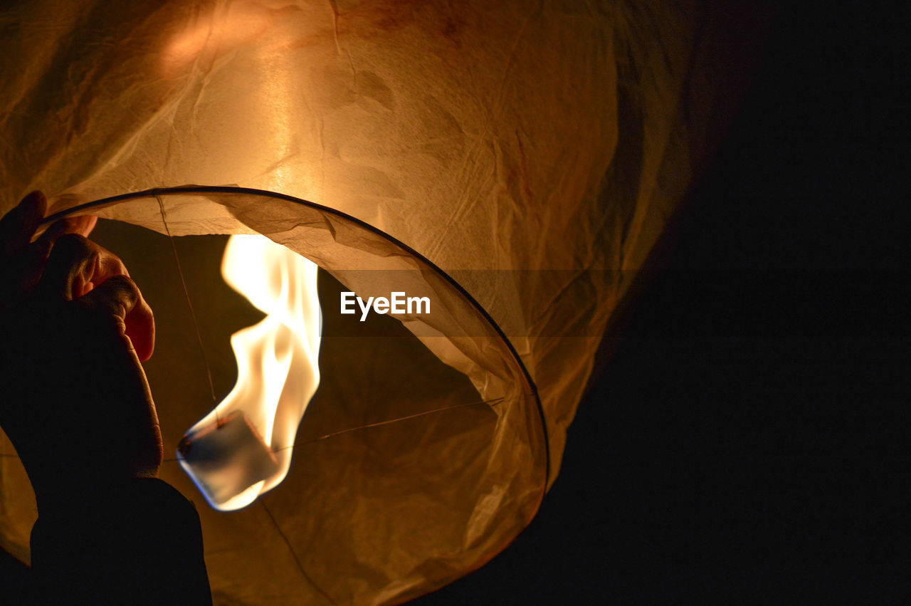 Cropped hand holding illuminated paper lantern at night