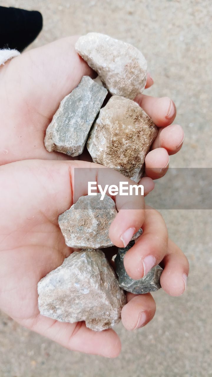 HIGH ANGLE VIEW OF PERSON HAND HOLDING STONES