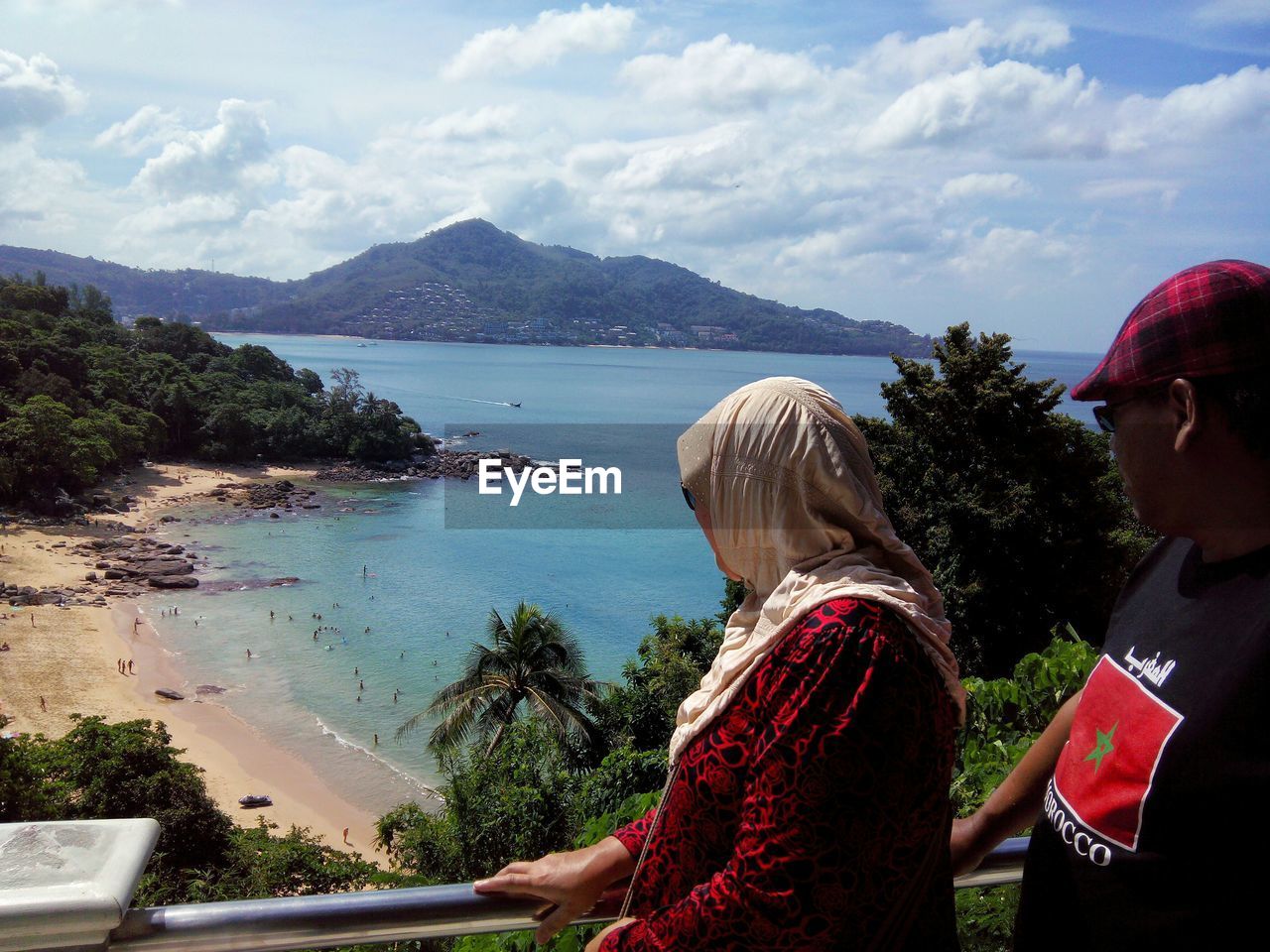REAR VIEW OF WOMAN LOOKING AT SEA AGAINST MOUNTAIN SKY