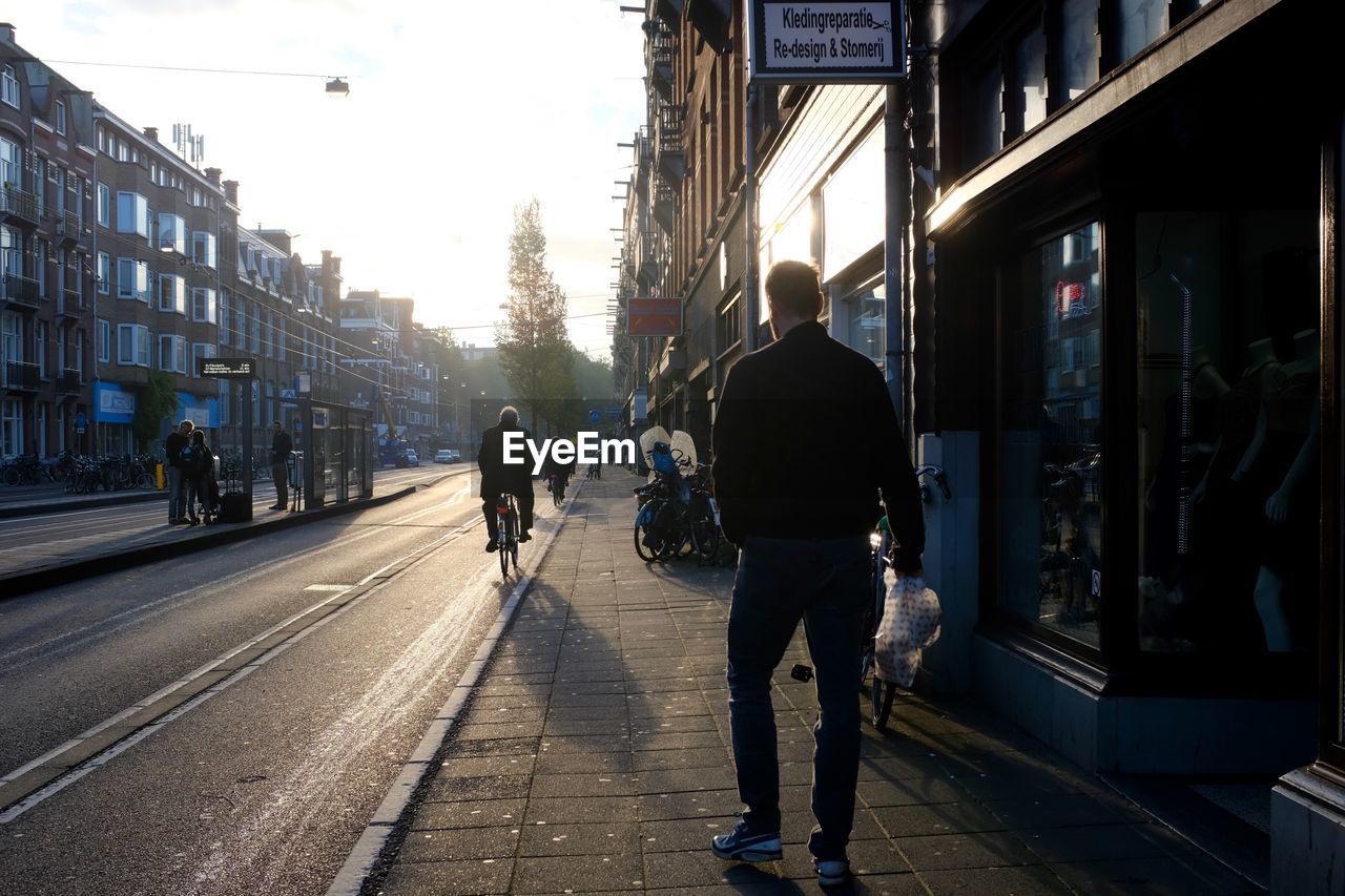 REAR VIEW OF PEOPLE WALKING ON STREET IN CITY