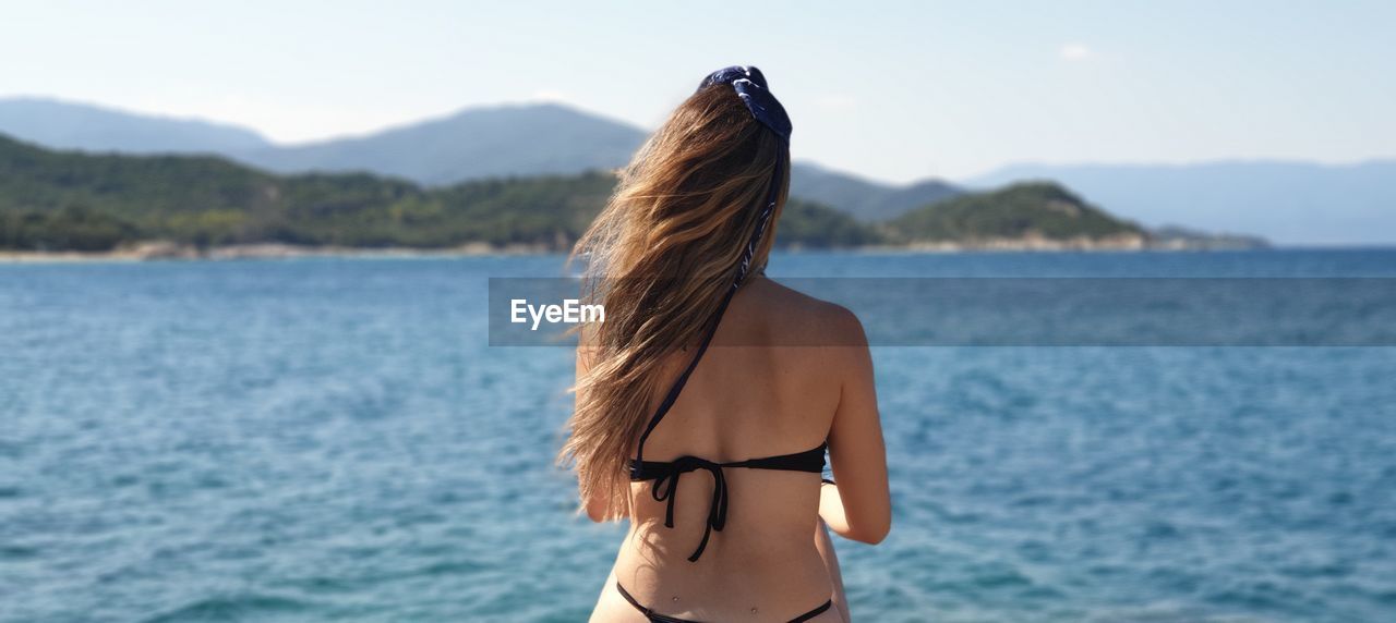 Rear view of woman in bikini standing against sea