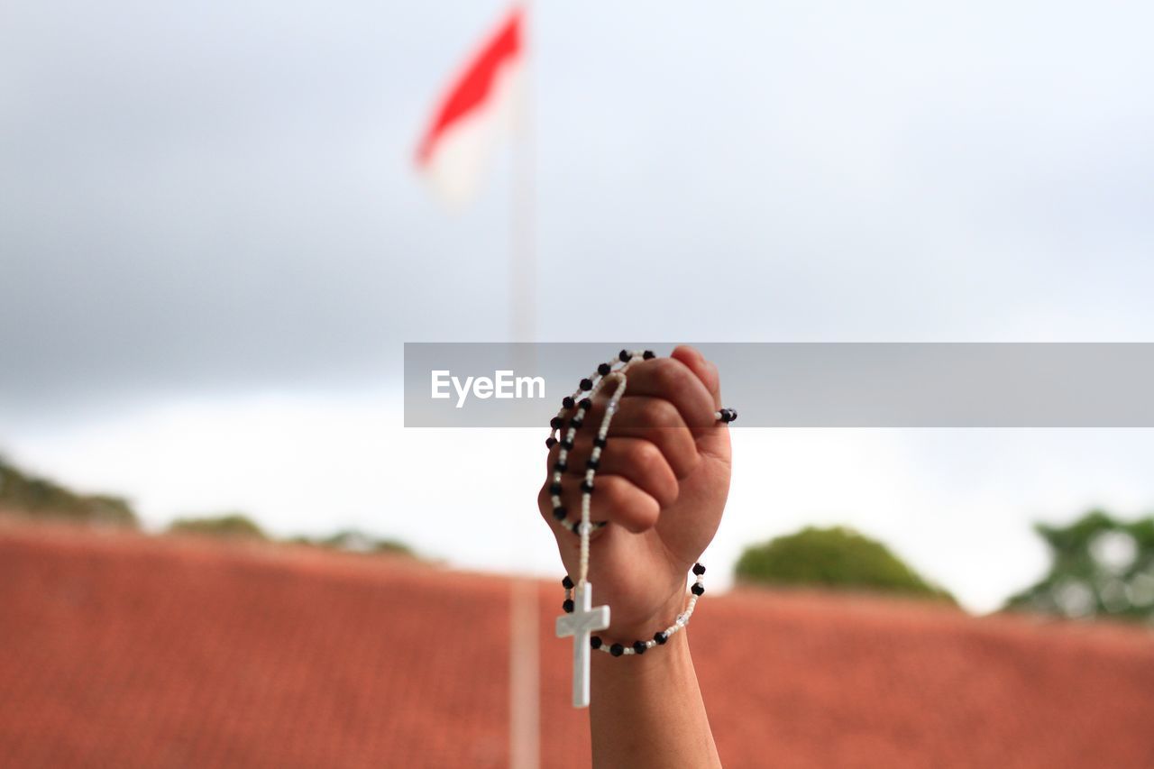 Close-up of hand holding prayer beads against flag