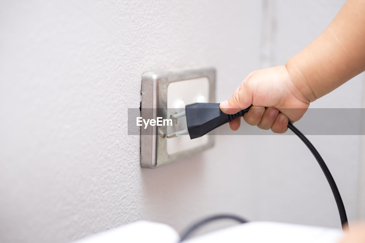 Cropped hand of boy inserting electric plug in electrical outlet at home