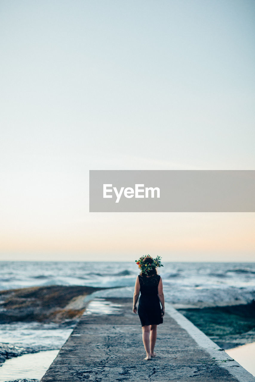 Rear view of woman on pier against sea during sunset