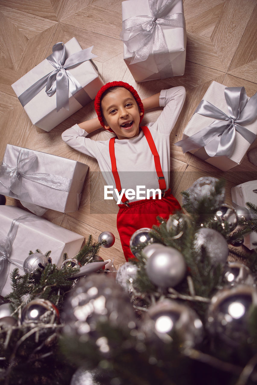 Merry christmas kid. child one boy lying on the floor under the tree amongst boxes of presents.