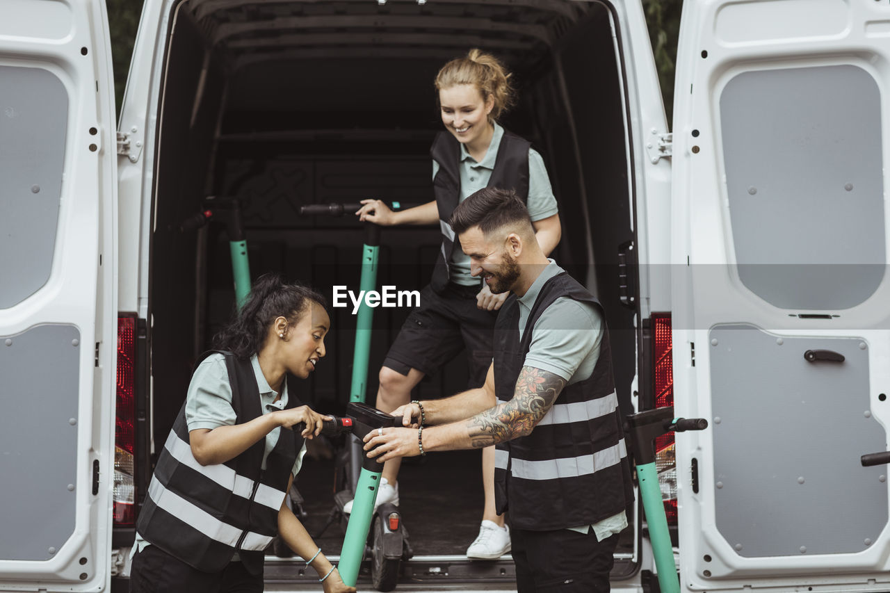 Smiling multiracial coworkers loading electric push scooter in delivery van