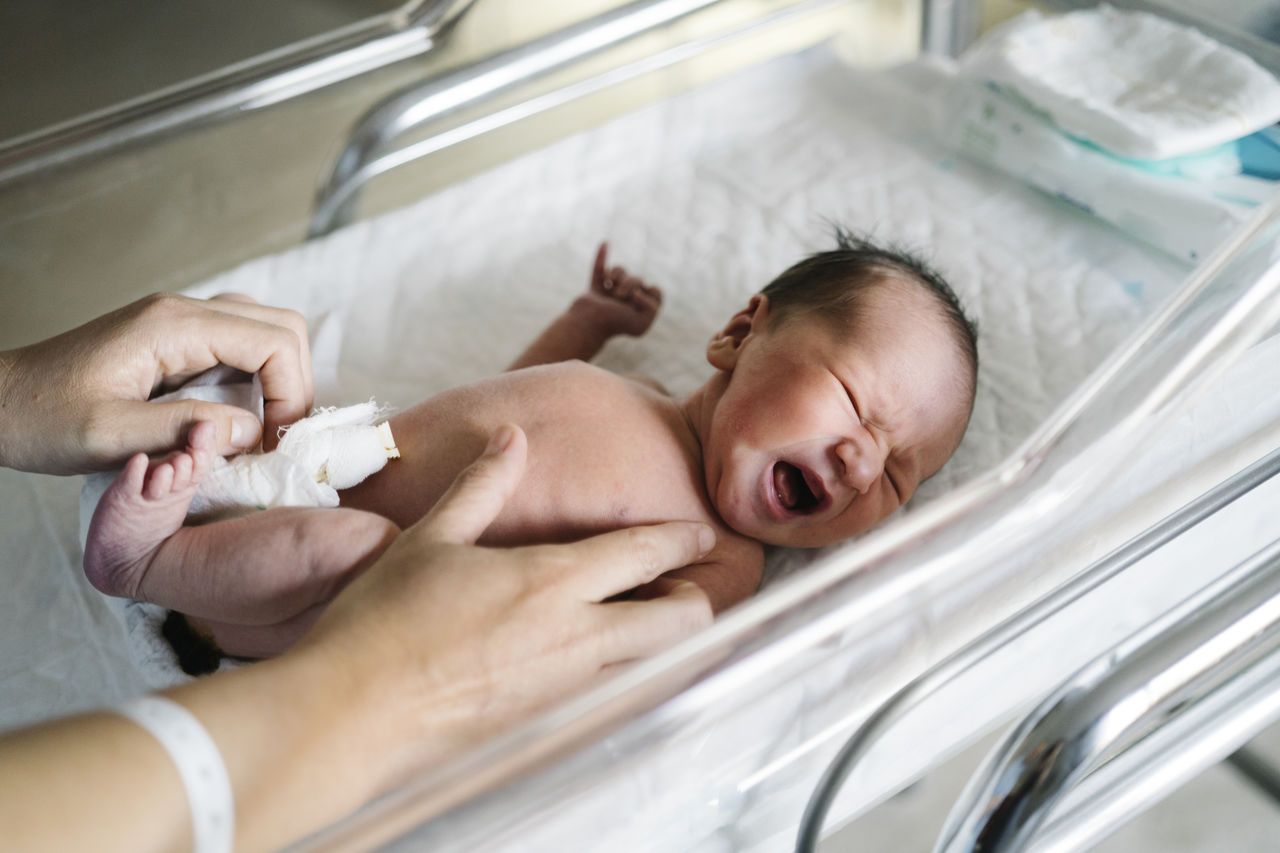 Woman changing crying baby boy diaper in hospital