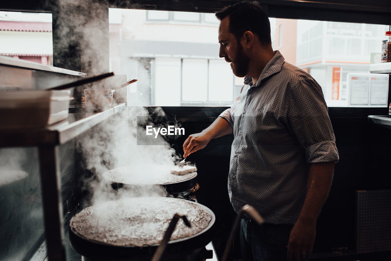 Male chef working in restaurant kitchen, buttering hot crepes