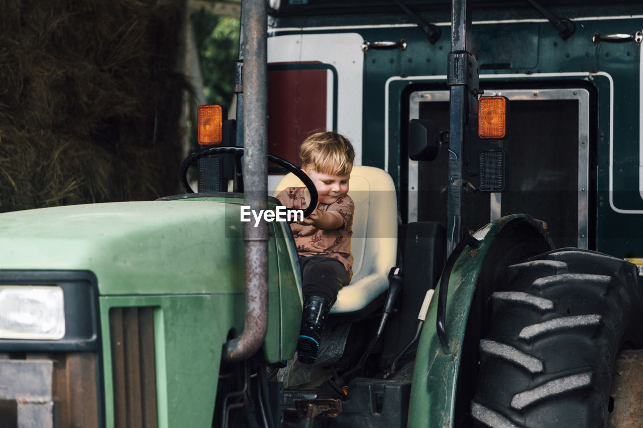 Happy boy sitting on tractor in farm