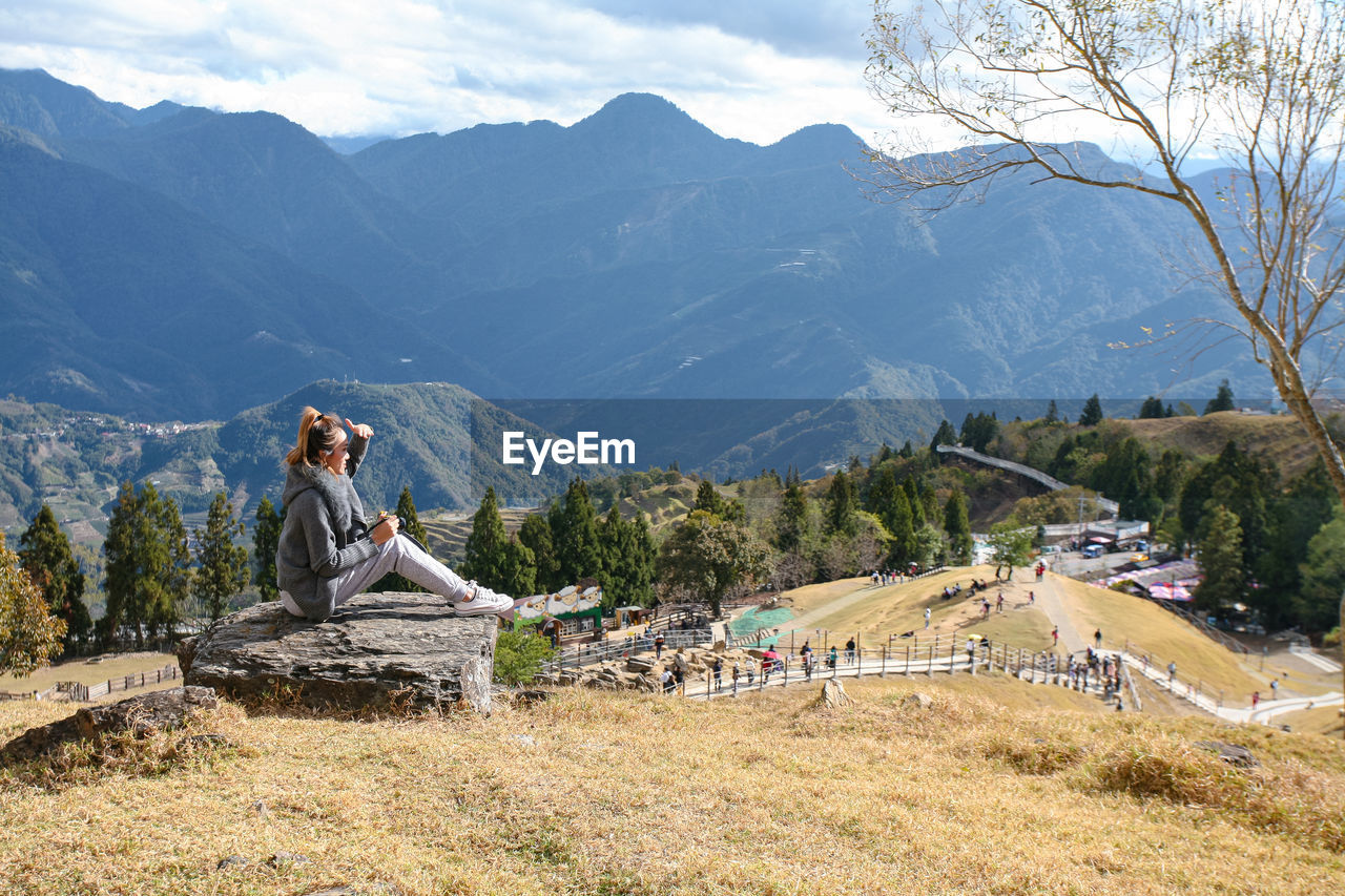 Woman shielding eyes while sitting on rock