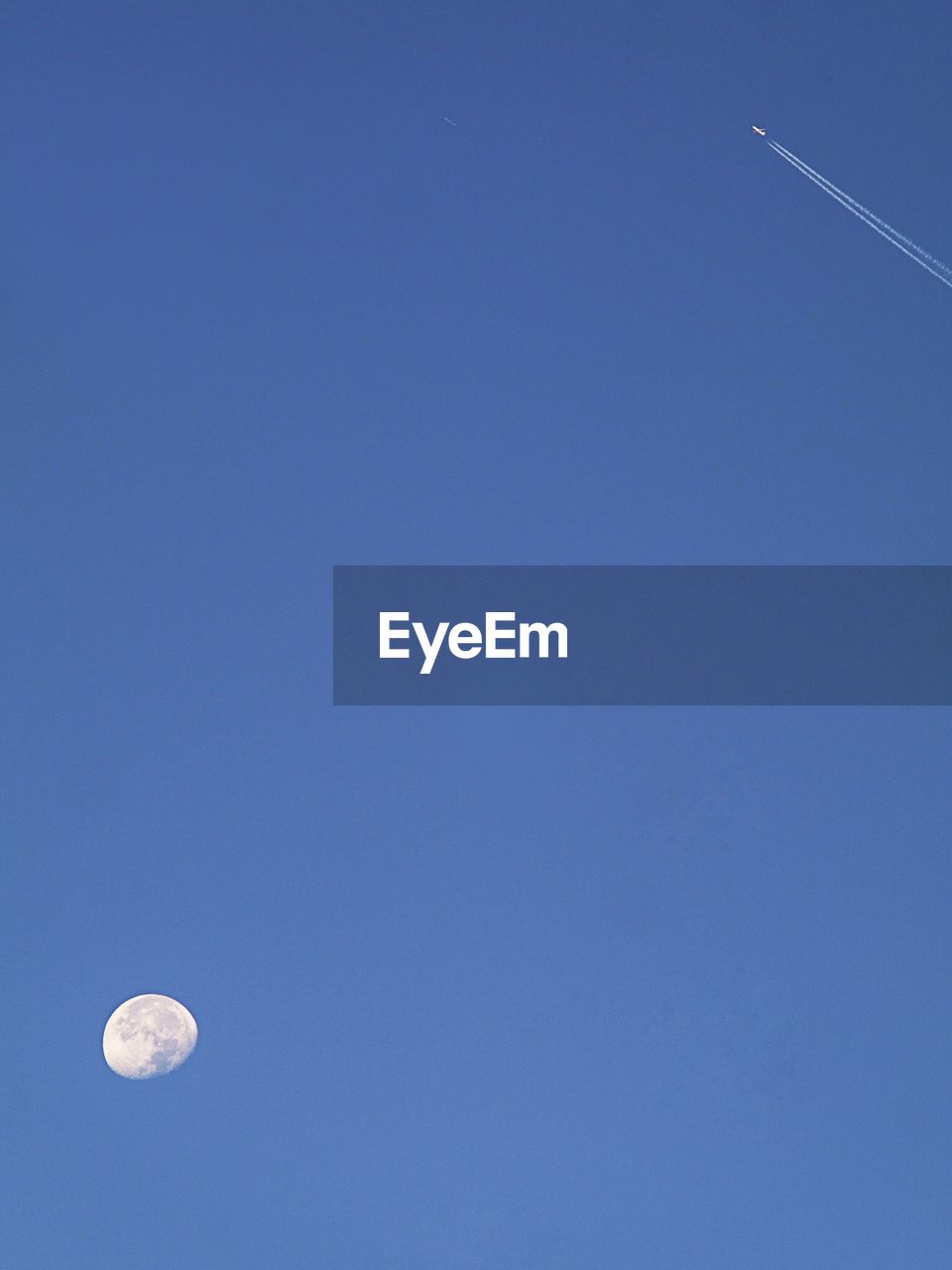 Low angle view of full moon and airplane in clear blue sky