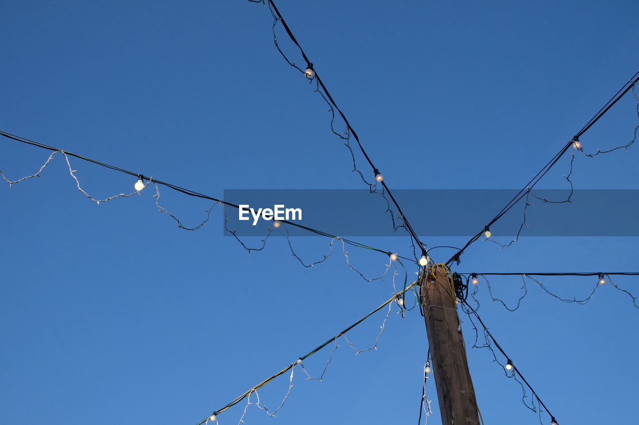 Low angle view of illuminated string light against clear blue sky