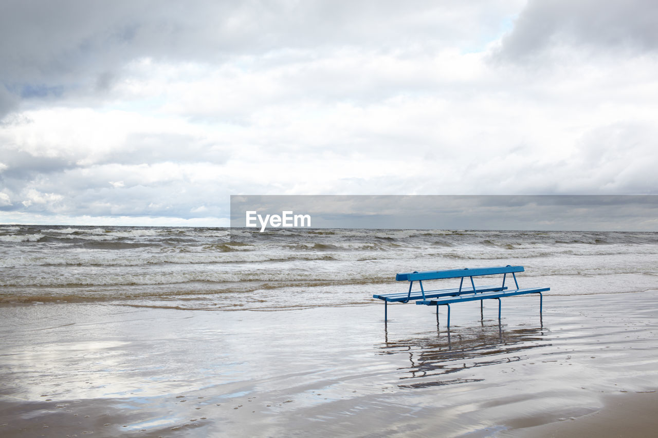 Empty bench at beach against sky