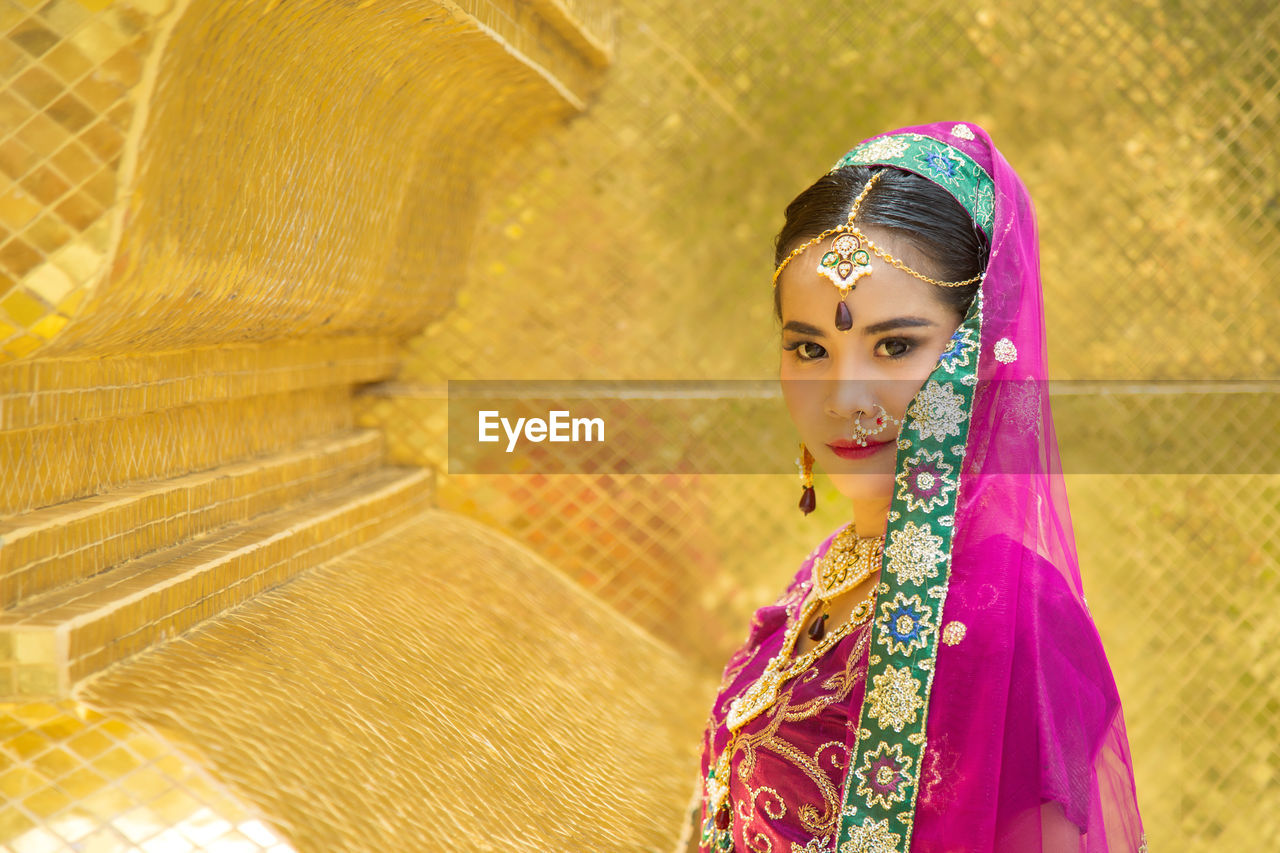  portrait asian woman in a purple indian traditional saree with a golden wall background.