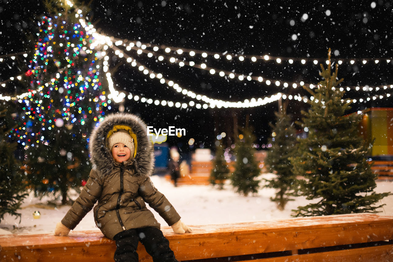 portrait of young woman standing against illuminated christmas tree at night