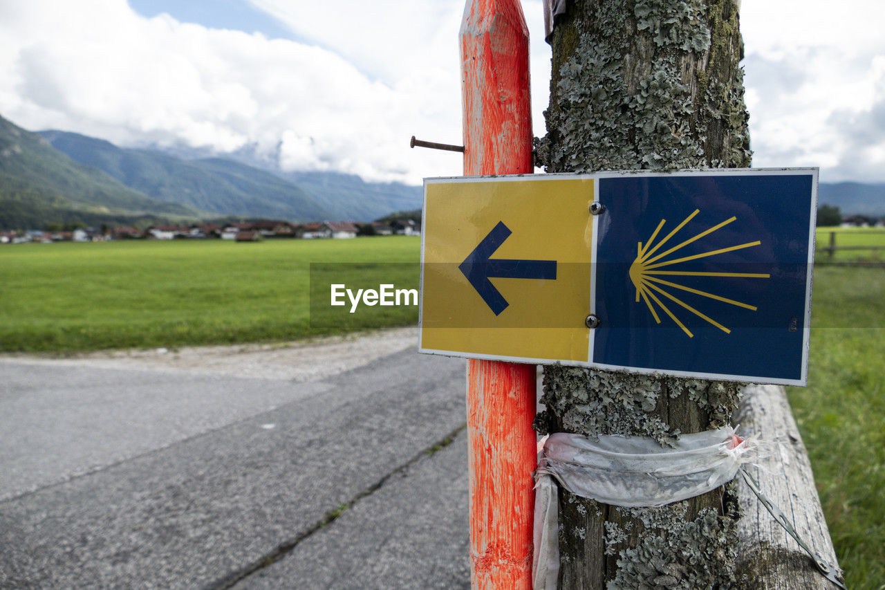 sign, road, nature, mountain, symbol, cloud, road sign, sky, transportation, guidance, communication, grass, plant, no people, day, landscape, arrow symbol, environment, directional sign, outdoors, traffic sign, mountain range, scenics - nature, information sign, land, tree, travel, non-urban scene, rural scene